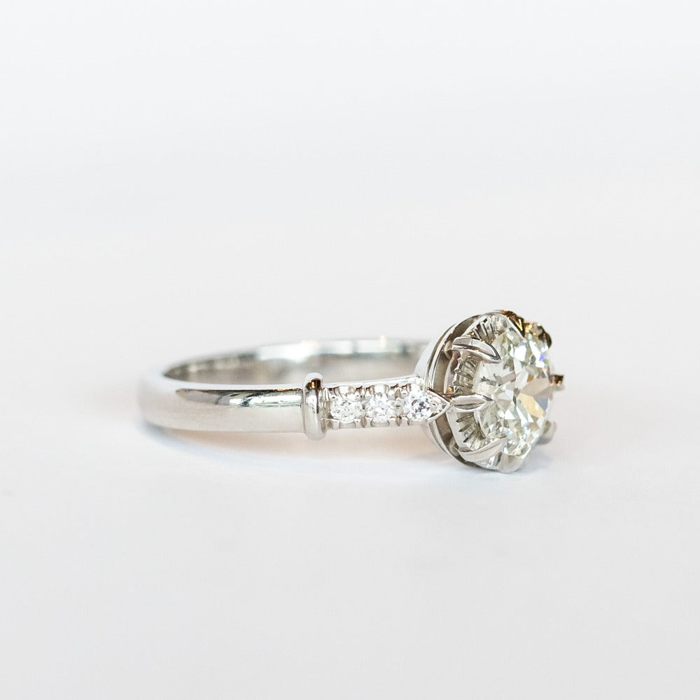A platinum engagement ring with a prong set old European cut diamond, cathedral shoulders, and three accent diamonds on each shoulder.