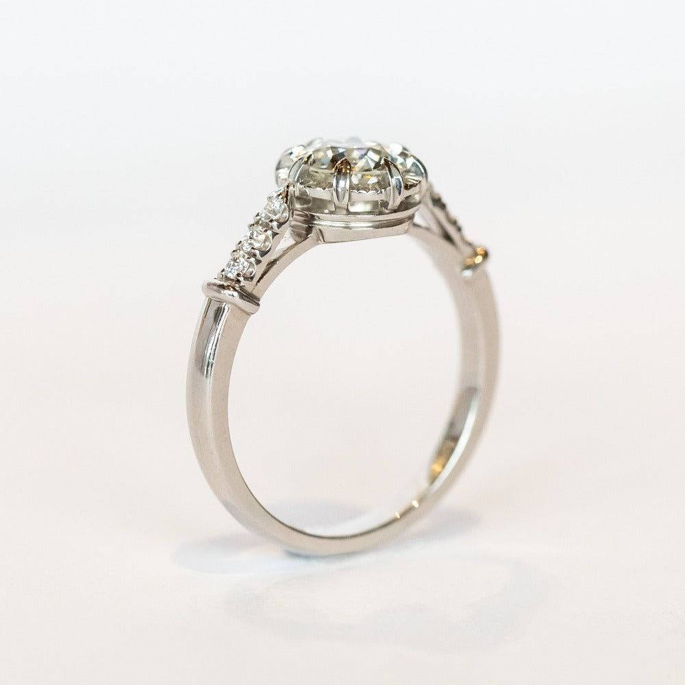 A platinum engagement ring with a prong set old European cut diamond, cathedral shoulders, and three accent diamonds on each shoulder.