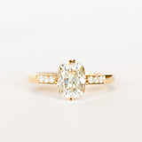 A yellow gold engagement ring set with a cushion cut diamond center stone in compass point double claw prongs, flanked by three small diamonds on each shoulder.