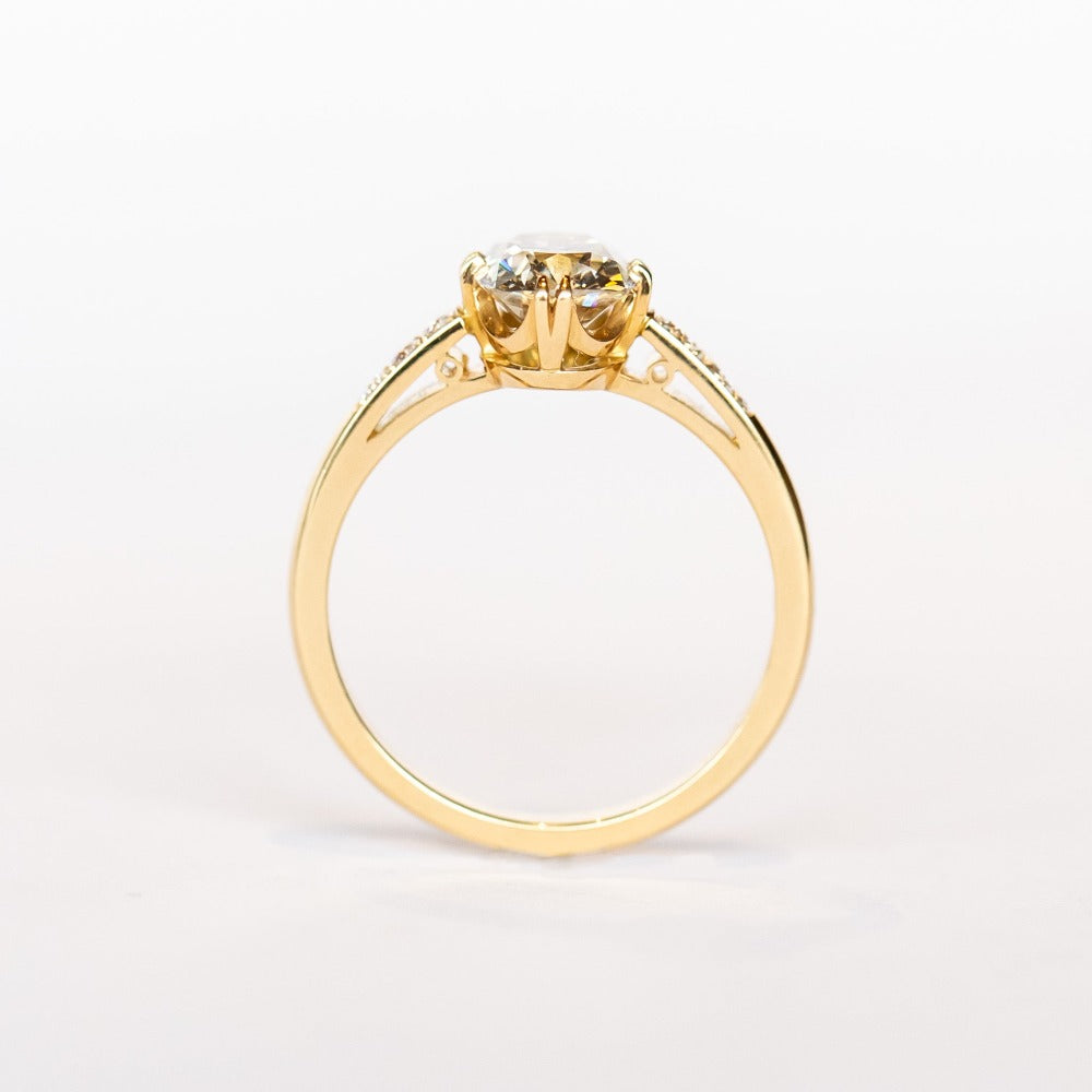 A yellow gold engagement ring set with a cushion cut diamond center stone in compass point double claw prongs, flanked by three small diamonds on each shoulder.