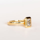 A yellow gold solitaire engagement ring featuring a bezel set rectangular step cut diamond.