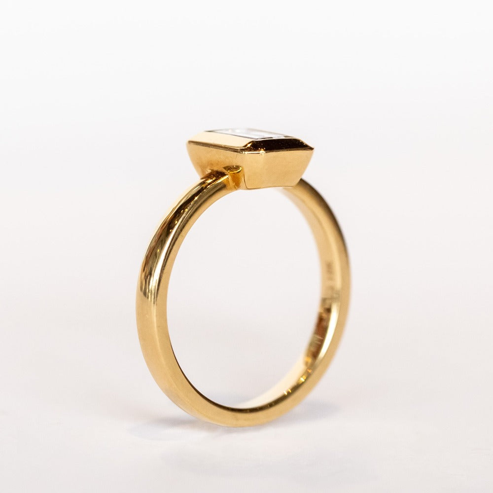 A yellow gold solitaire engagement ring featuring a bezel set rectangular step cut diamond.