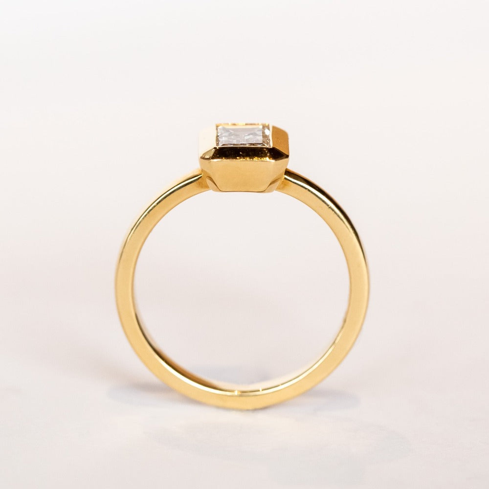 A yellow gold solitaire engagement ring featuring a bezel set rectangular step cut diamond.