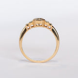 A rose gold engagement ring featuring a bezel set emerald cut diamond center stone flanked by two vertically set baguette diamonds in graduating sizes on either side.