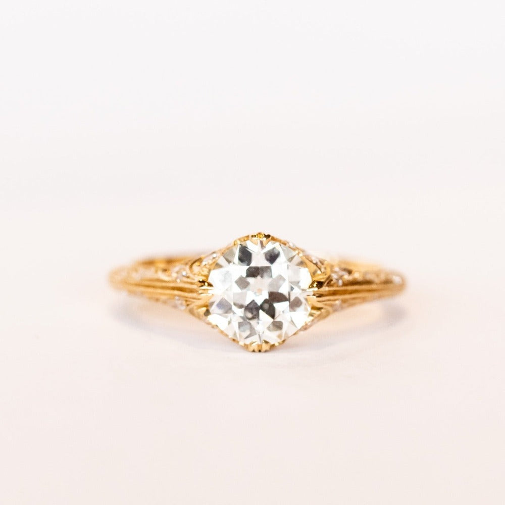 An old European cut diamond engagement ring in yellow gold with filigree accents and several side stones set into the shoulders.