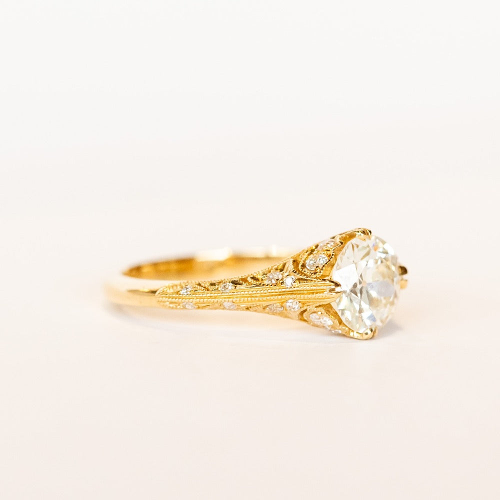 An old European cut diamond engagement ring in yellow gold with filigree accents and several side stones set into the shoulders.