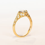 An old European cut diamond engagement ring in yellow gold with filigree accents and several side stones set into the shoulders.