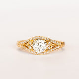 A yellow gold engagement ring that features an old European cut center diamond, floral filigree accents, and rows of pave diamonds.