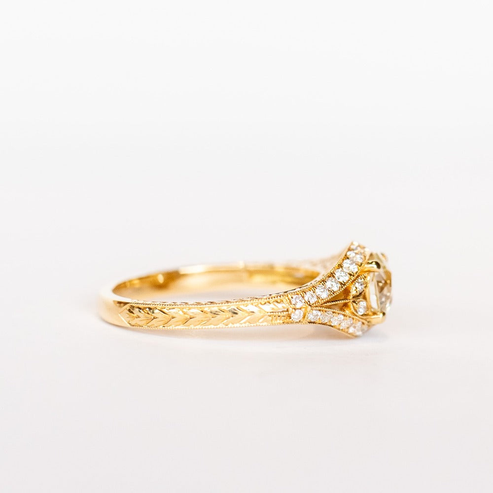 A yellow gold engagement ring that features an old European cut center diamond, floral filigree accents, and rows of pave diamonds.