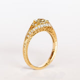 A yellow gold engagement ring that features an old European cut center diamond, floral filigree accents, and rows of pave diamonds.