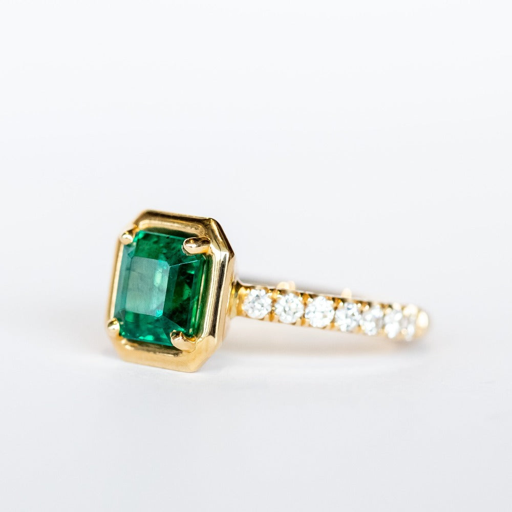 An engagement ring with an Asscher cut center emerald gemstone in yellow gold with accent diamonds on each shoulder of the ring.