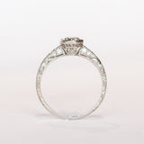 A platinum diamond engraved engagement ring with a bezel set old mine cut diamond center stone and a few diamond accents on each shoulder.
