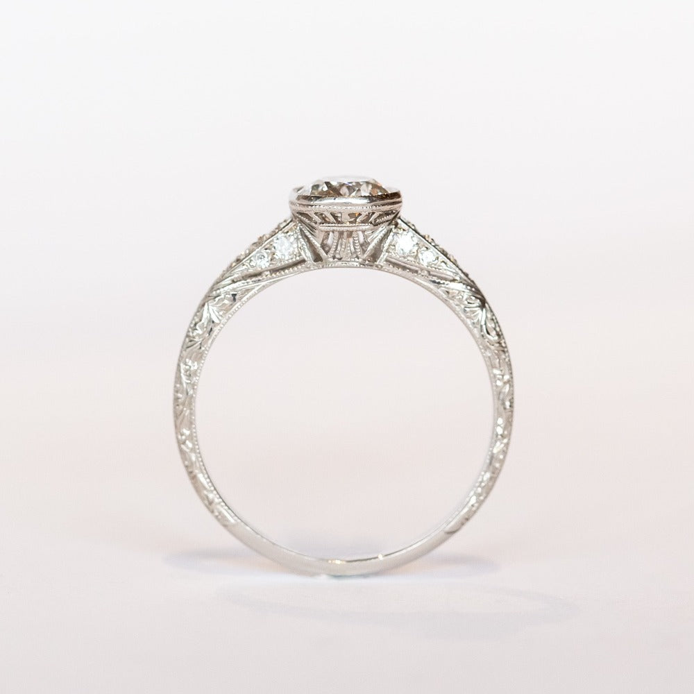 A platinum diamond engraved engagement ring with a bezel set old mine cut diamond center stone and a few diamond accents on each shoulder.