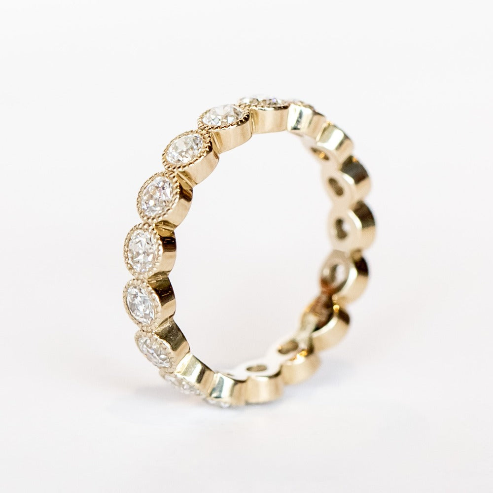 A white gold and diamond eternity band with bezel set old European cut diamonds and milgrain accents.