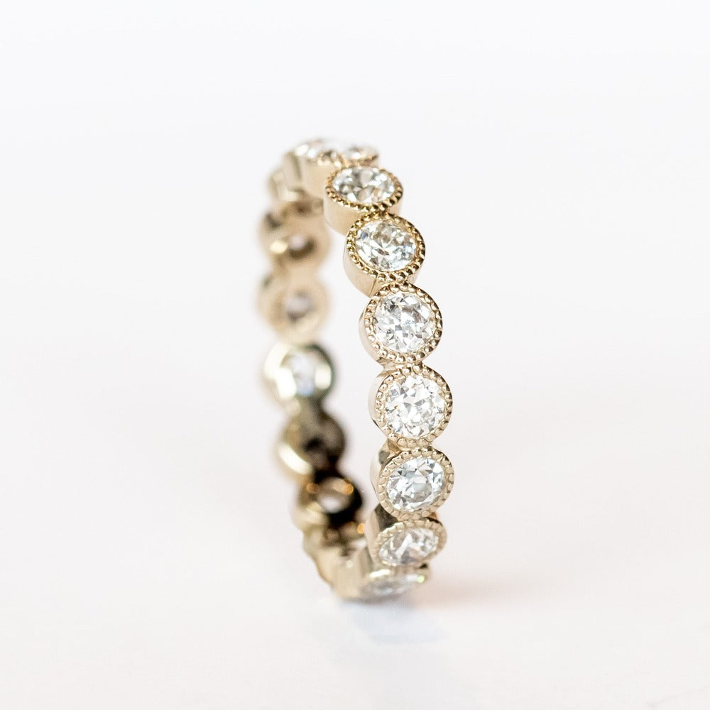 A white gold and diamond eternity band with bezel set old European cut diamonds and milgrain accents.