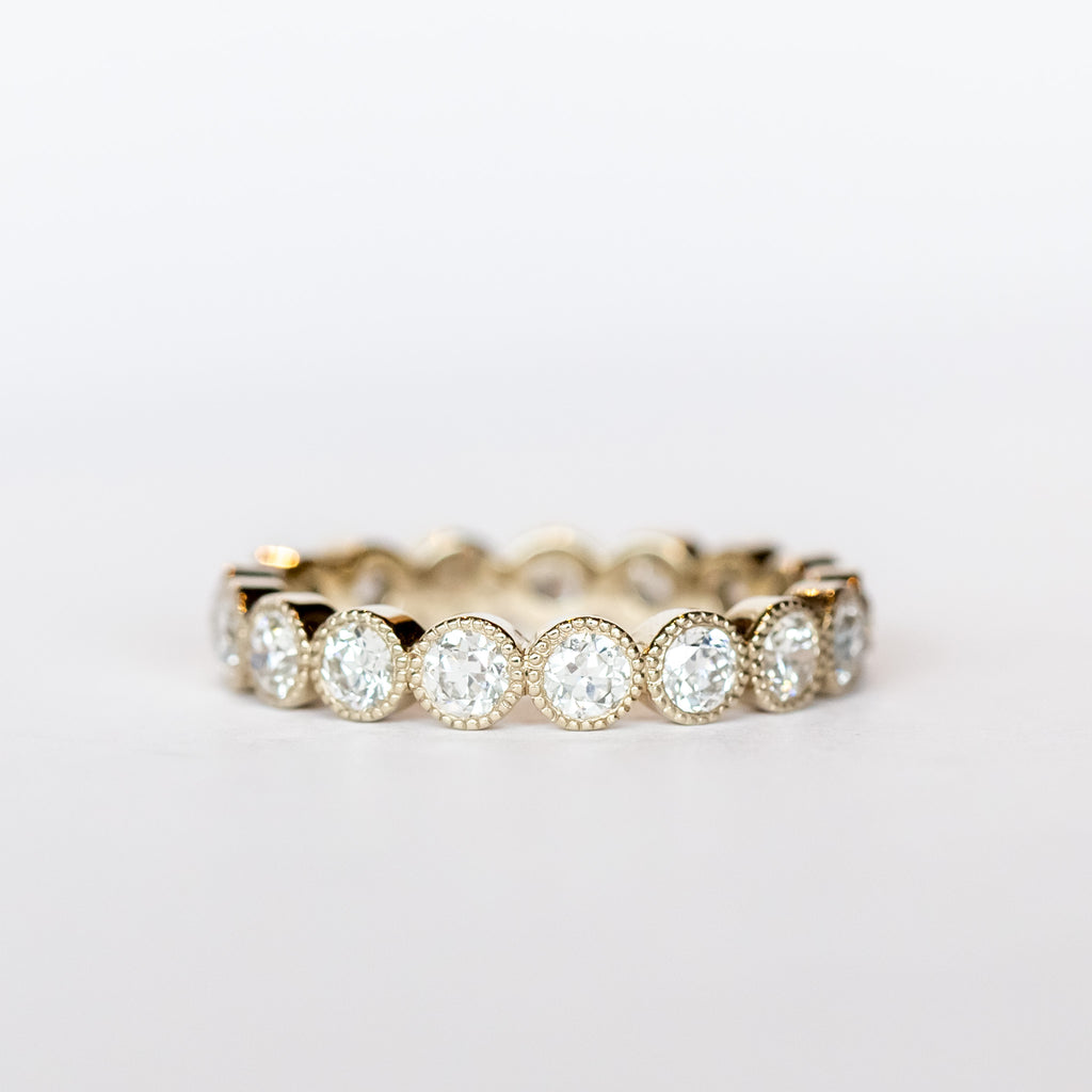 A white gold and diamond eternity band with bezel set old European cut diamonds and milgrain accents.