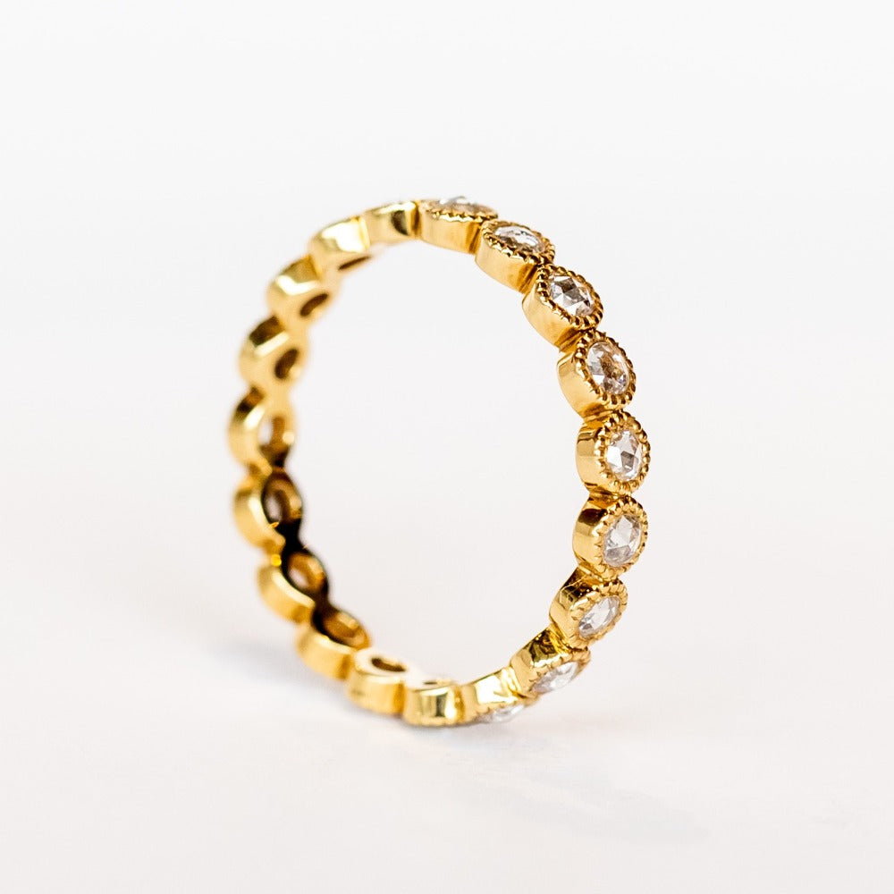 A yellow gold and diamond eternity band with rose cut round diamonds bezel set with milgrain edges.