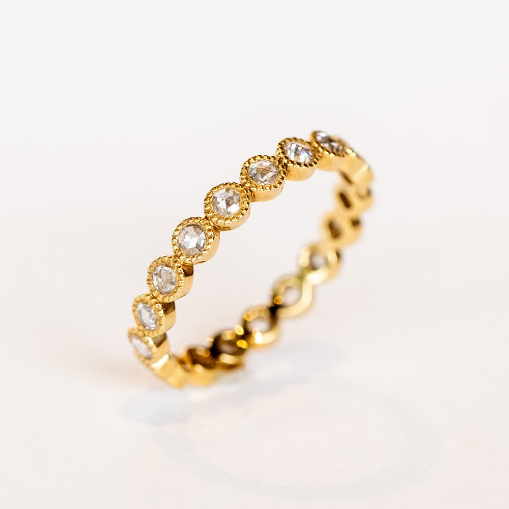 A yellow gold and diamond eternity band with rose cut round diamonds bezel set with milgrain edges.