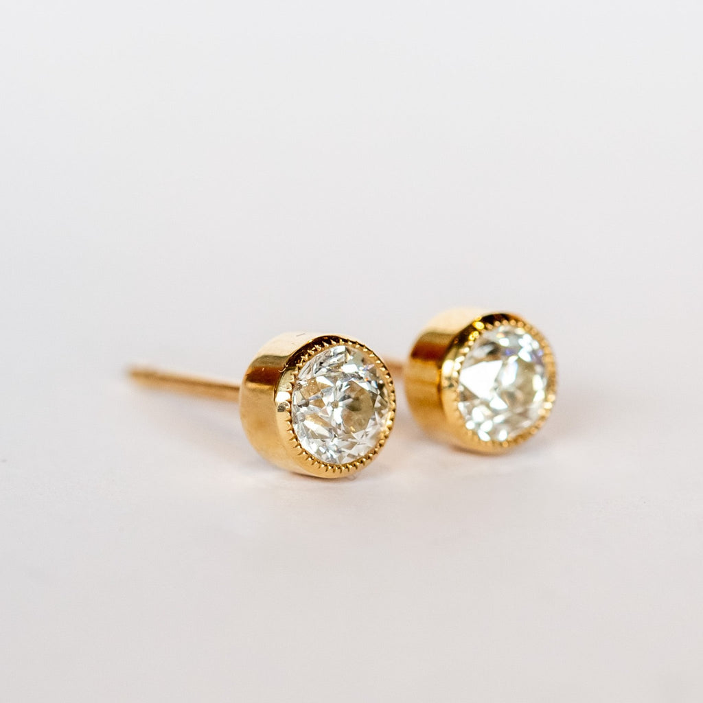 Old European cut diamond stud earrings set in yellow gold bezels with milgrain edges.