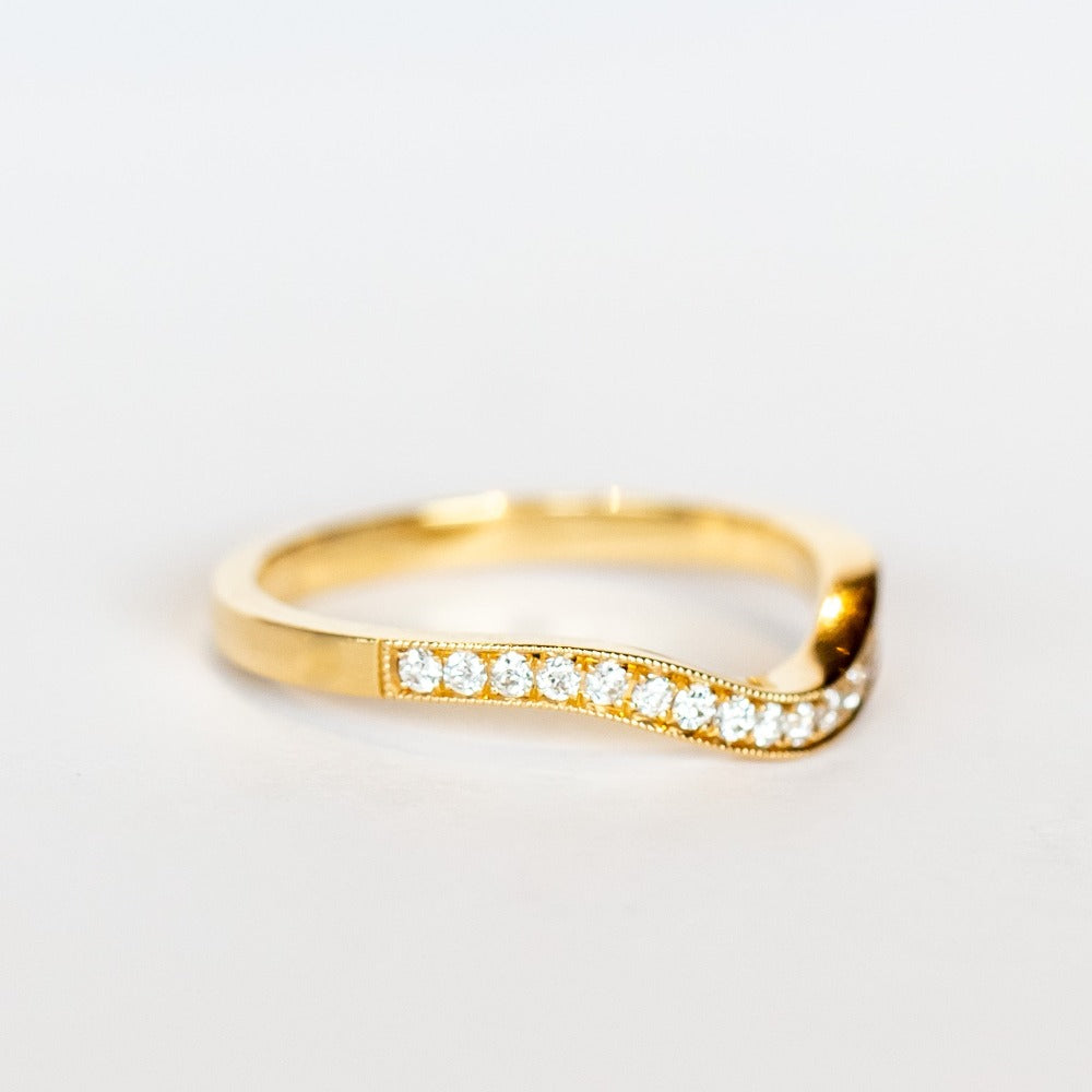 A contour curved yellow gold wedding band with a row of petite diamonds along the top.