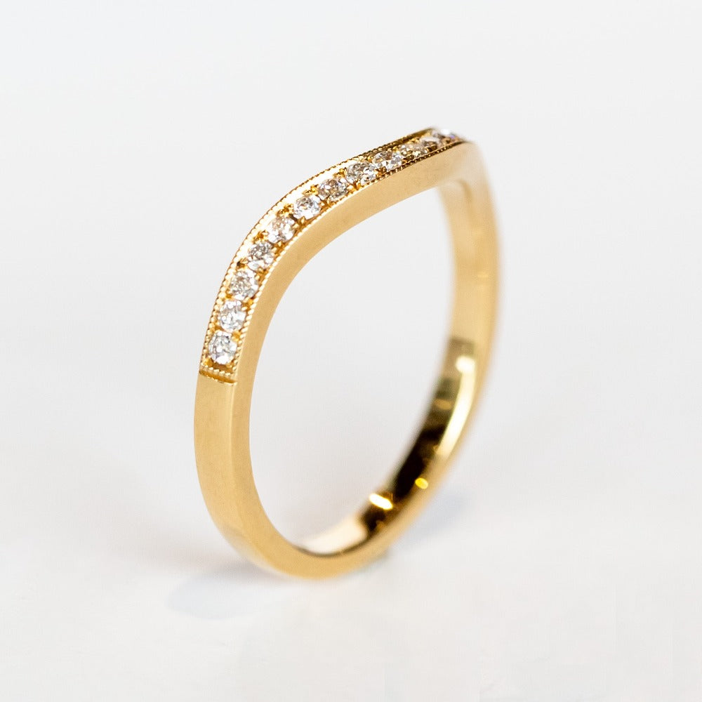 A contour curved yellow gold wedding band with a row of petite diamonds along the top.