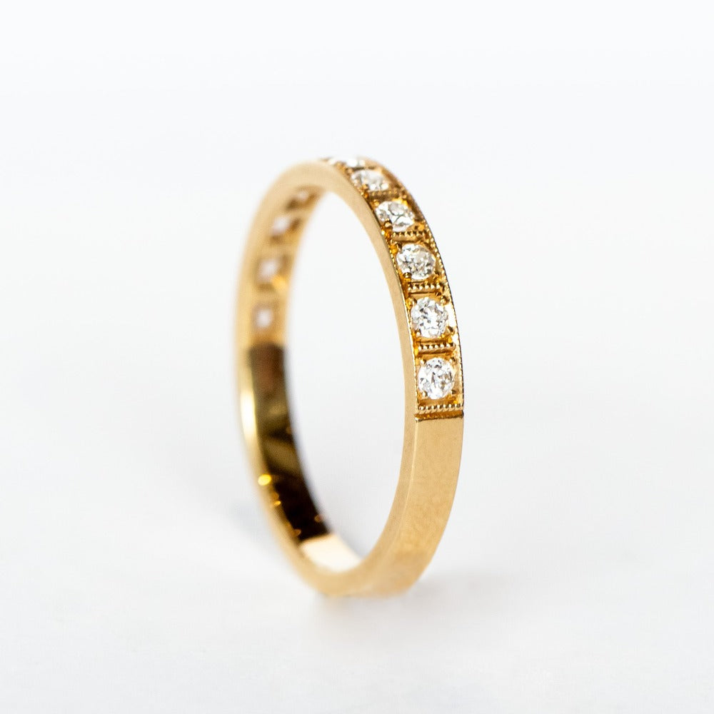 A yellow gold wedding band with a row of round old European cut diamonds, pave set around half of the band, with milgrain accents on each side and in between in a square pattern.