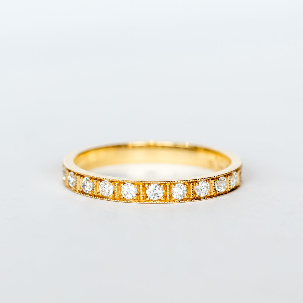 A yellow gold wedding band with a row of round old European cut diamonds, pave set around half of the band, with milgrain accents on each side and in between in a square pattern.