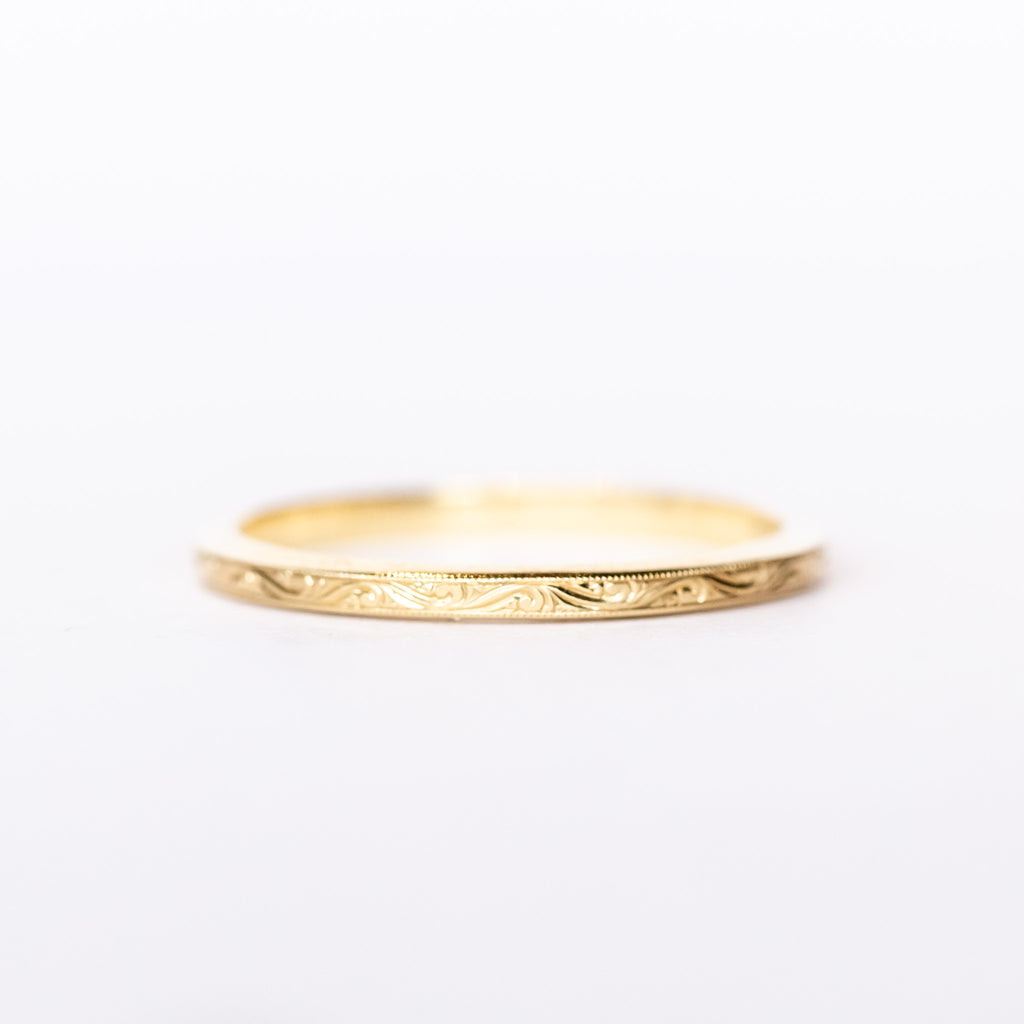 A thin, engraved yellow gold wedding band.
