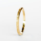 A thin, engraved yellow gold wedding band.