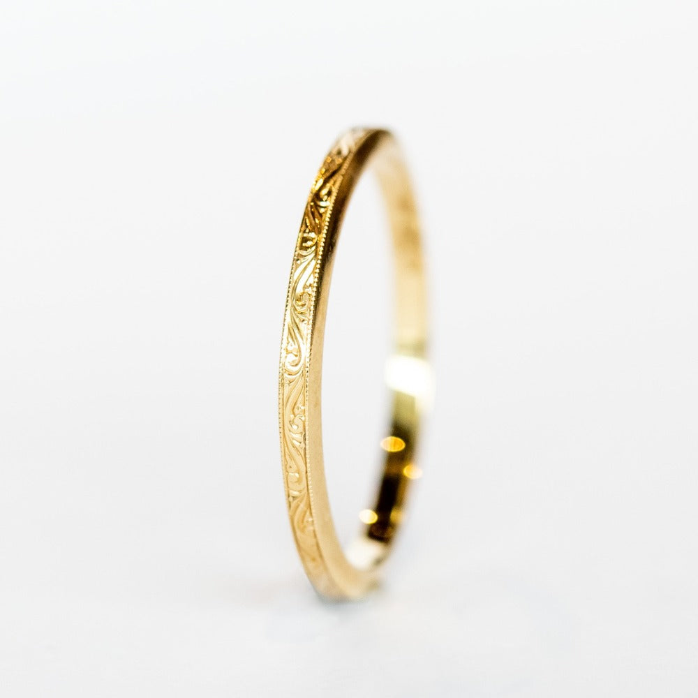 A thin, engraved yellow gold wedding band.