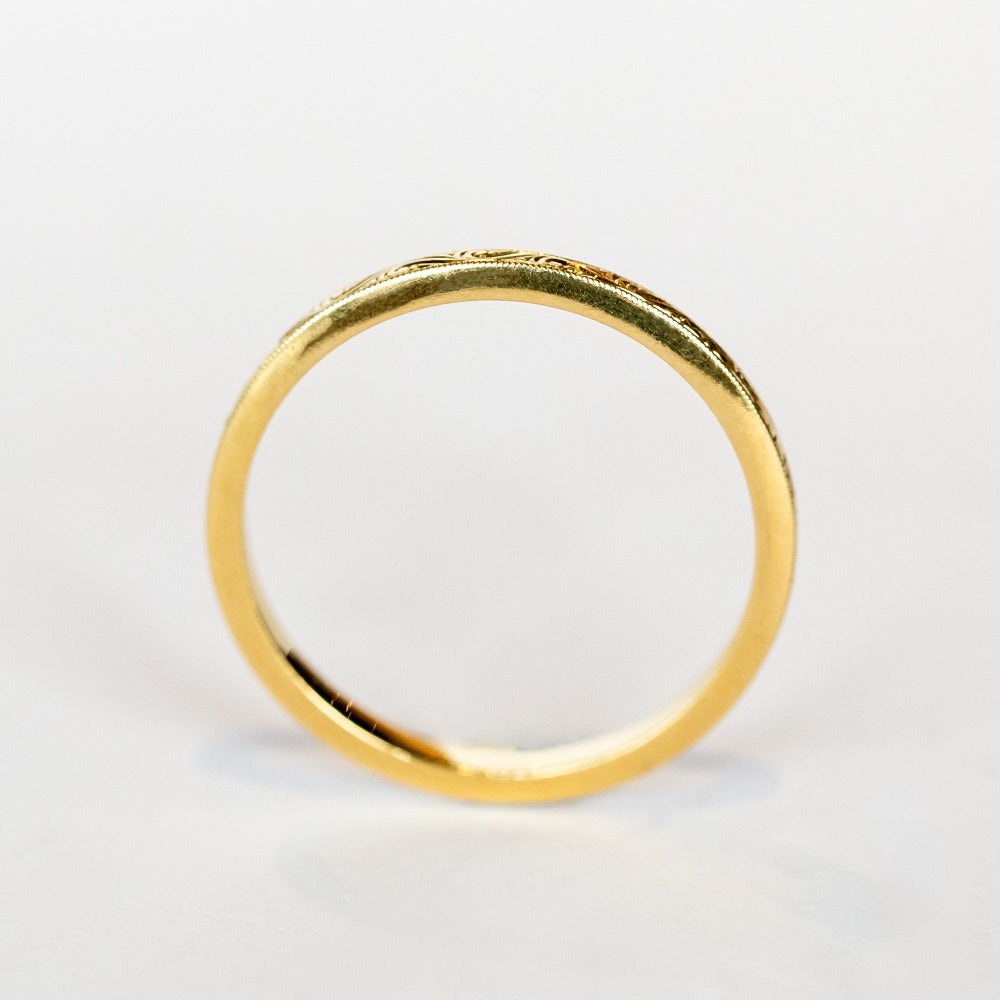 A thin, engraved yellow gold wedding band.