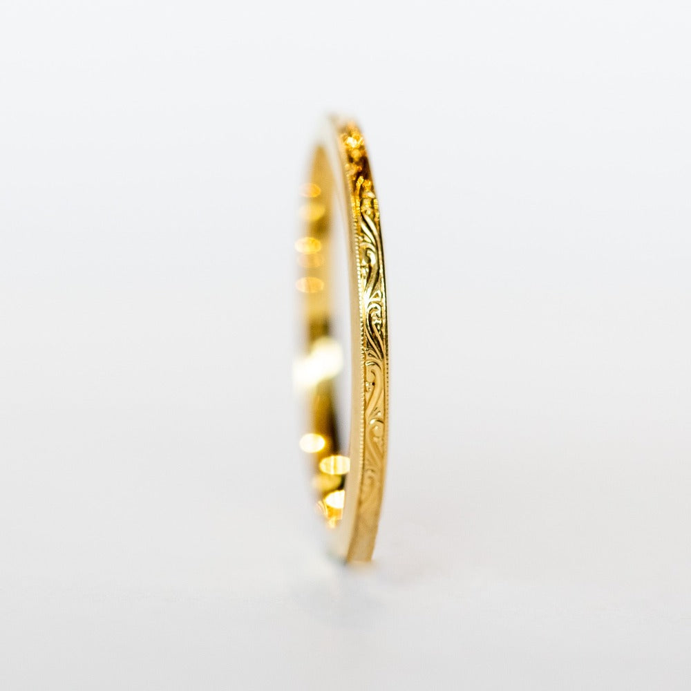 A thin, engraved yellow gold wedding band.