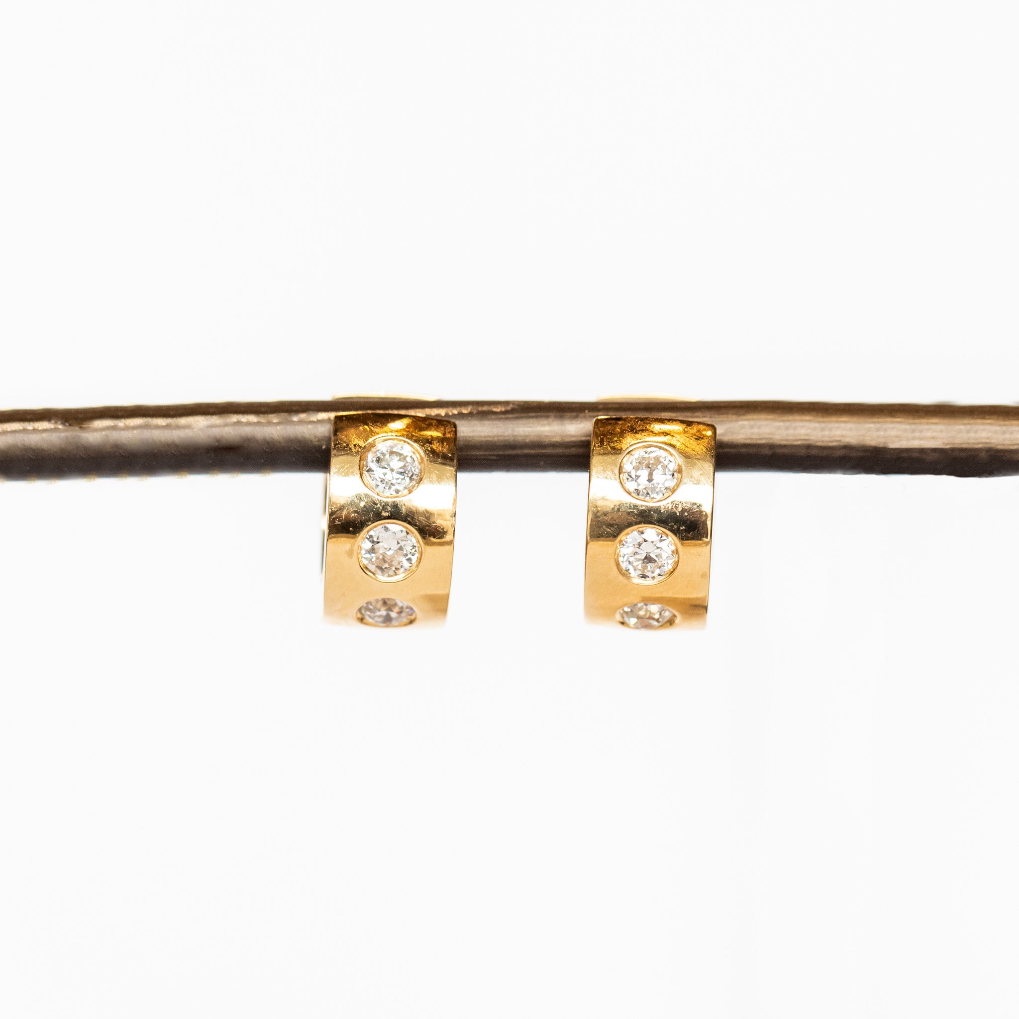 Yellow gold wide huggie hoop earrings set with three round burnished set diamonds down the front.