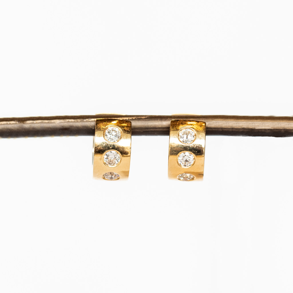 Yellow gold wide huggie hoop earrings set with three round burnished set diamonds down the front.