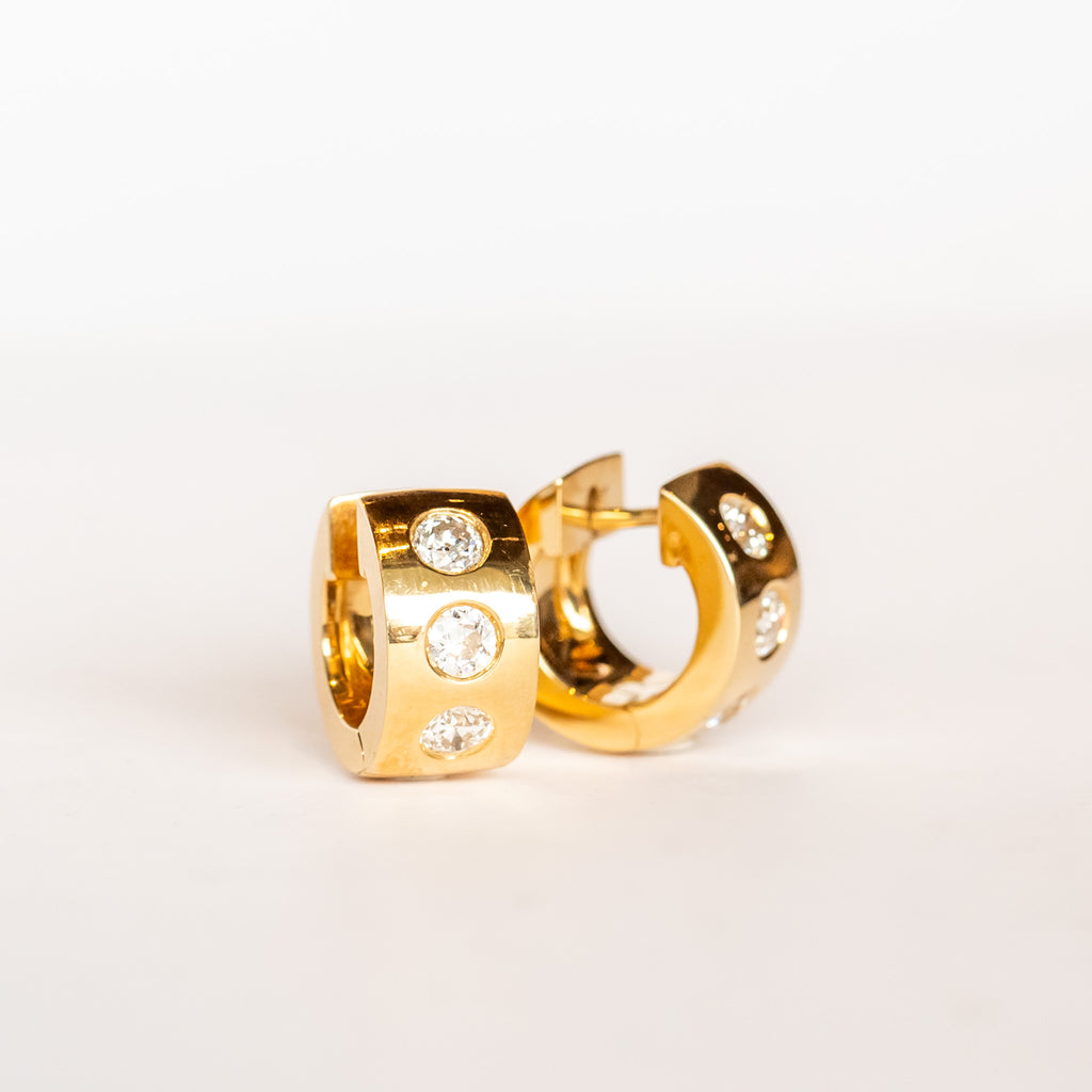 Yellow gold wide huggie hoop earrings set with three round burnished set diamonds down the front.