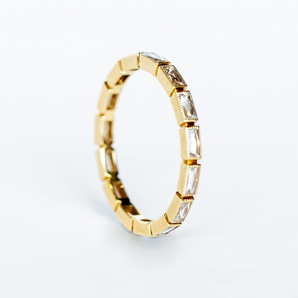 A yellow gold eternity band made up of bezel set, rectangular French cut diamonds.