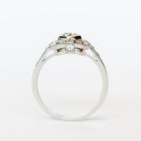 A platinum engagement ring featuring a bezel set central old European cut diamond framed by a square halo with milgrain details and diamond side stones with diamonds down each shoulder.