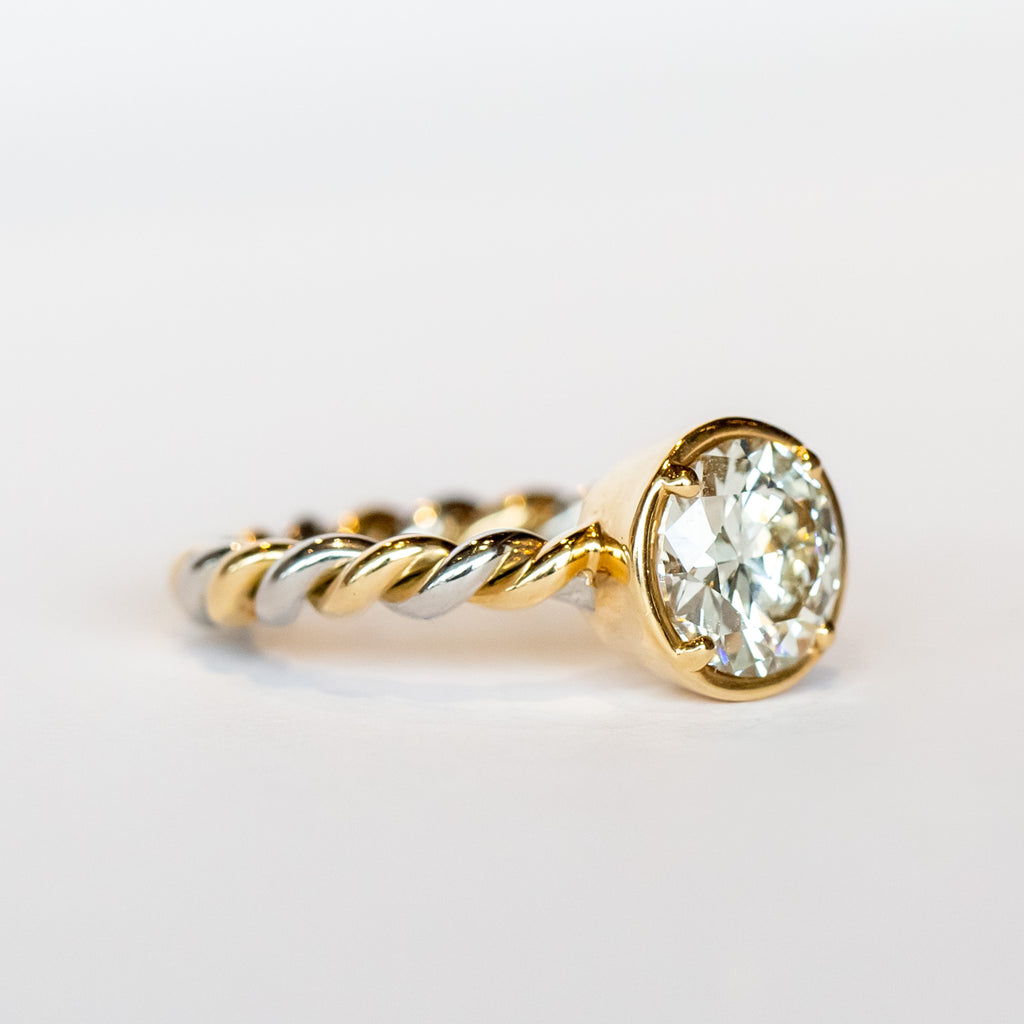 A diamond engagement ring featuring a prong set old European cut diamond on a twisted platinum and gold band.