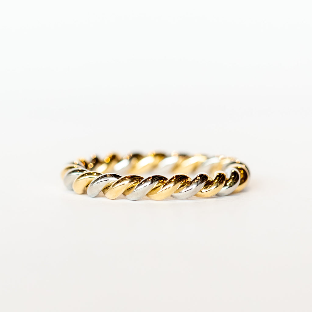 A wedding band made up of one platinum and one yellow gold strands twisted together with a polished finish.