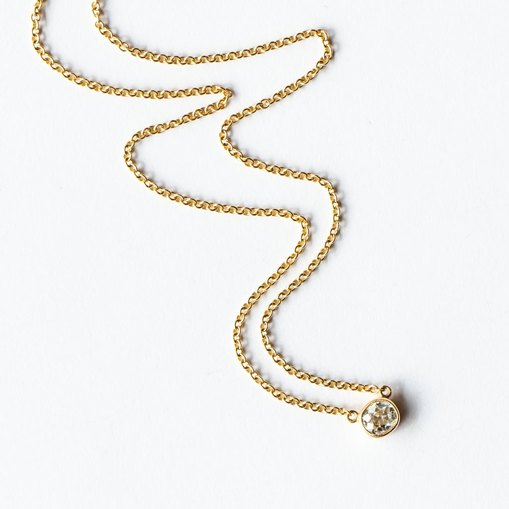 A bezel set cushion cut diamond in yellow gold on a cable chain necklace.