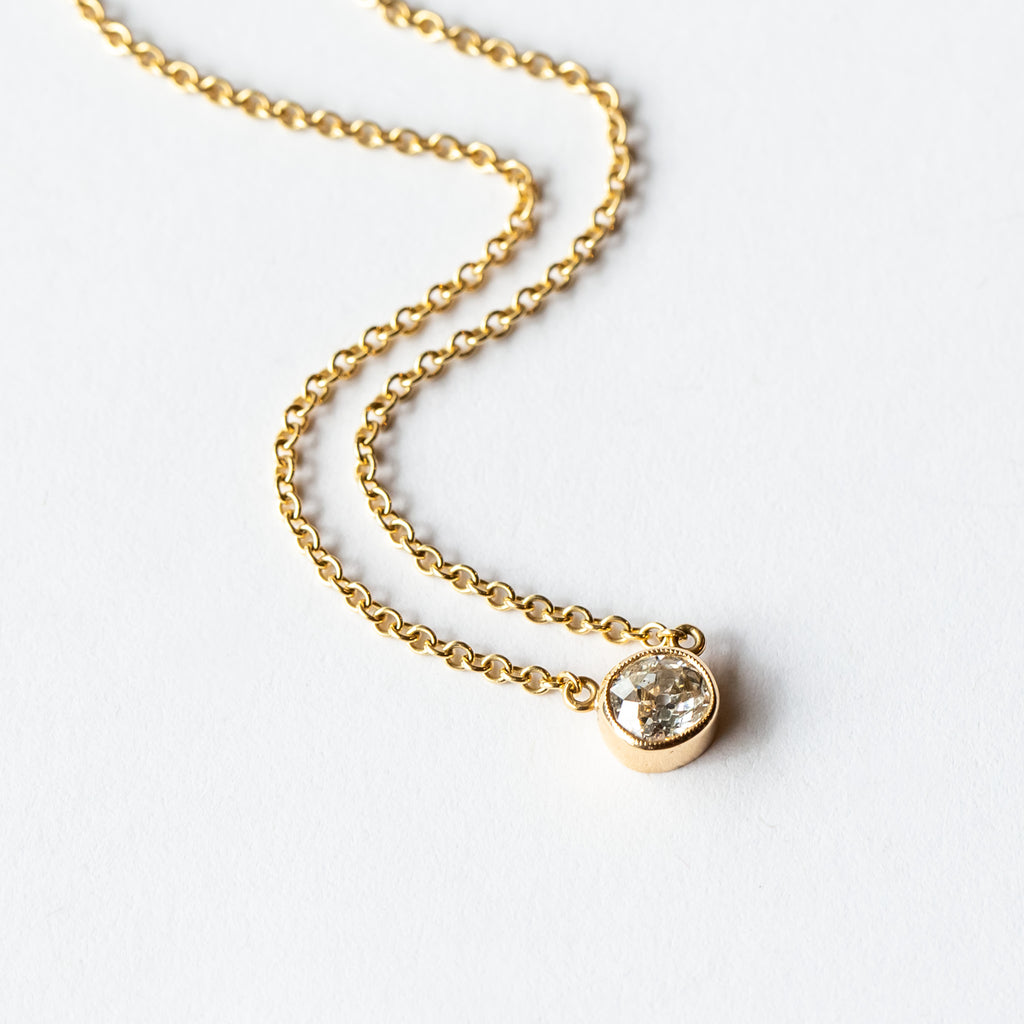 A bezel set cushion cut diamond in yellow gold on a cable chain necklace.