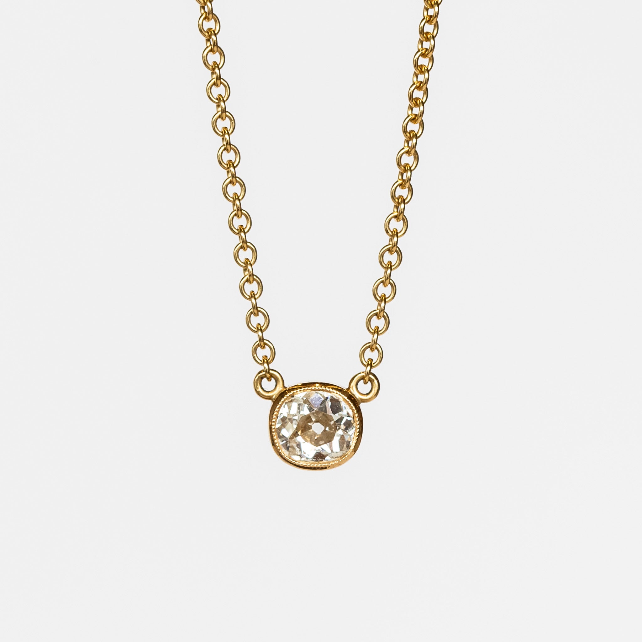 A bezel set cushion cut diamond in yellow gold on a cable chain necklace.