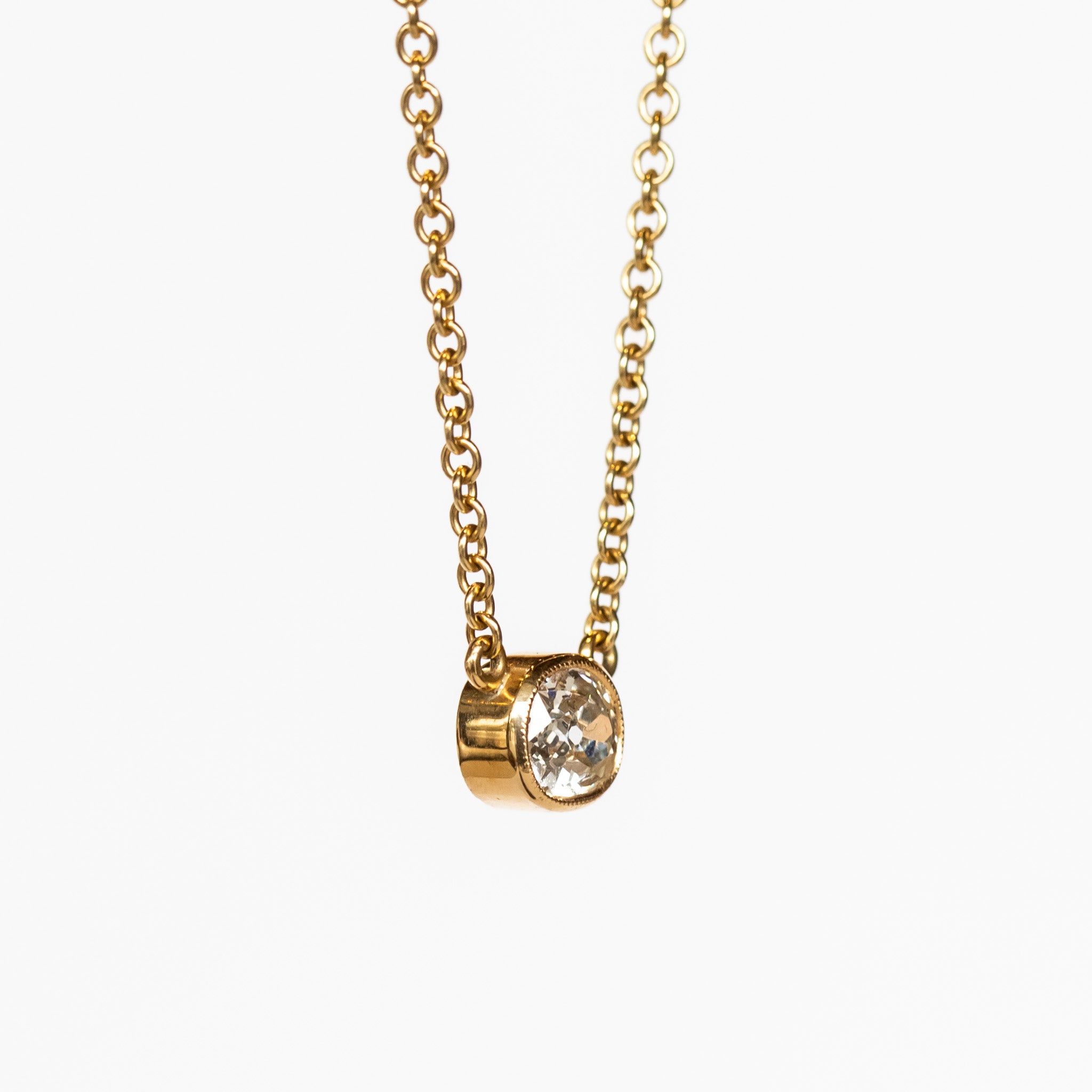 A bezel set cushion cut diamond in yellow gold on a cable chain necklace.