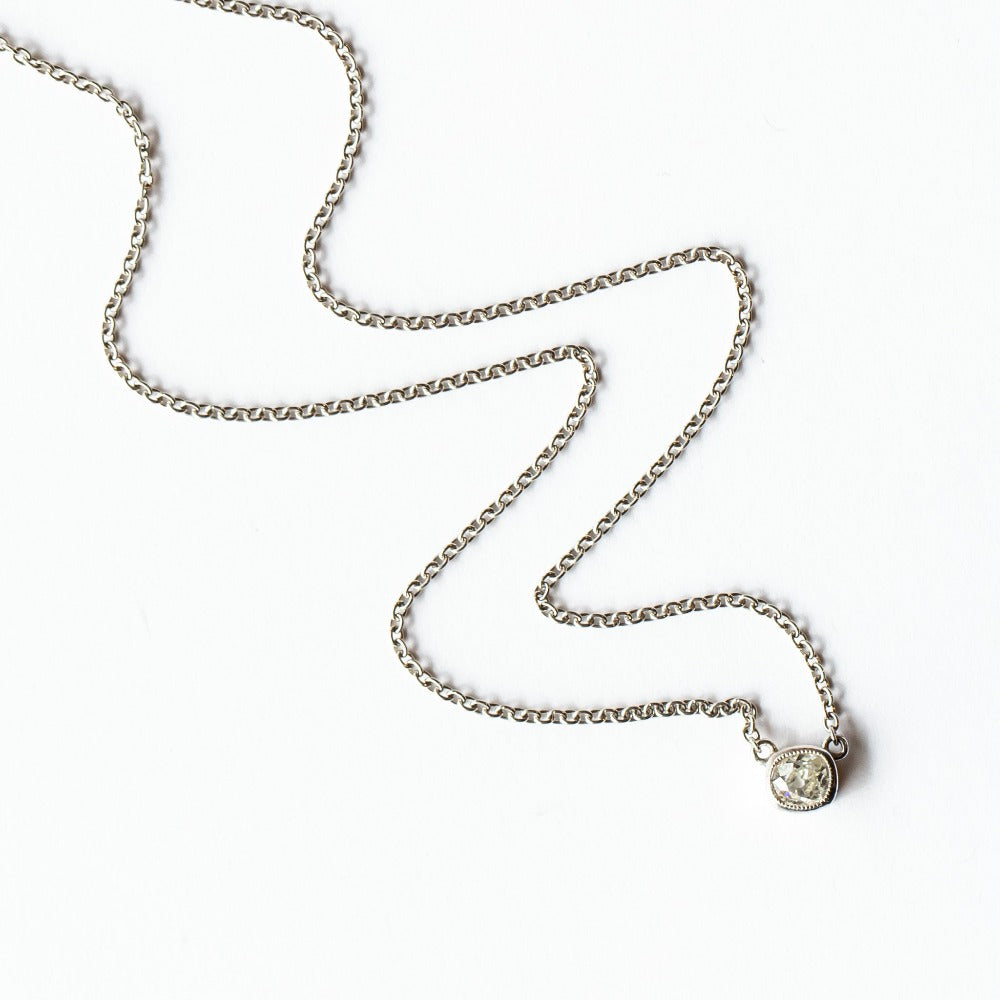 A cushion cut diamond in a platinum bezel setting with milgrain edge, stationed at the center of a platinum cable chain necklace.