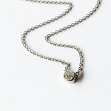 A cushion cut diamond in a platinum bezel setting with milgrain edge, stationed at the center of a platinum cable chain necklace.