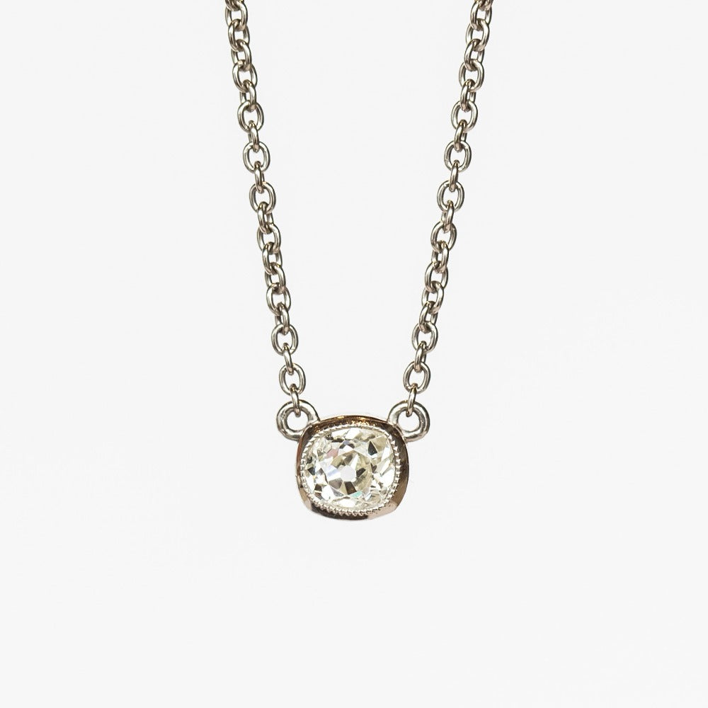 A cushion cut diamond in a platinum bezel setting with milgrain edge, stationed at the center of a platinum cable chain necklace.