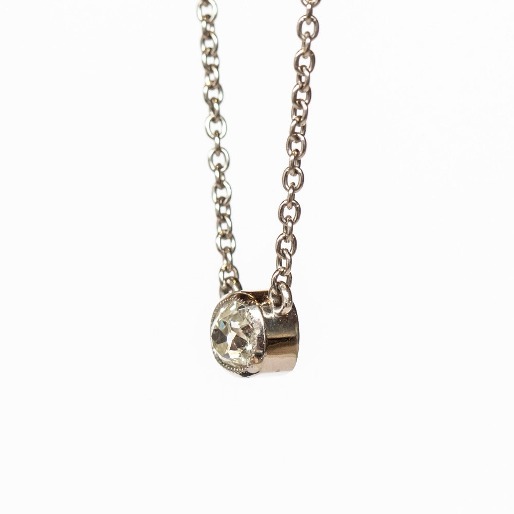 A cushion cut diamond in a platinum bezel setting with milgrain edge, stationed at the center of a platinum cable chain necklace.