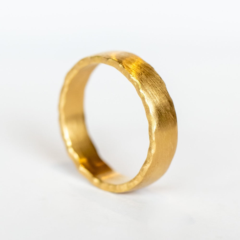A wide, yellow gold wedding band with brushed matte finish and torn-paper like edges.