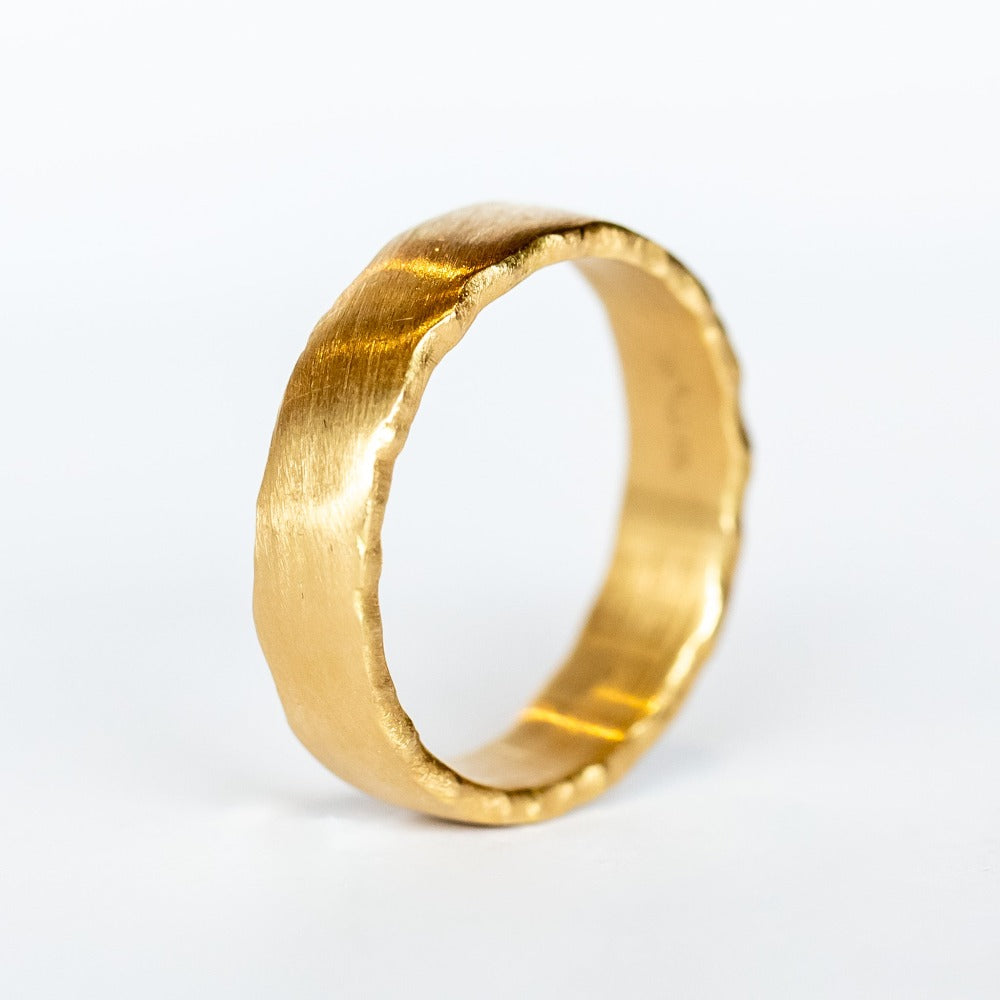A wide, yellow gold wedding band with brushed matte finish and torn-paper like edges.