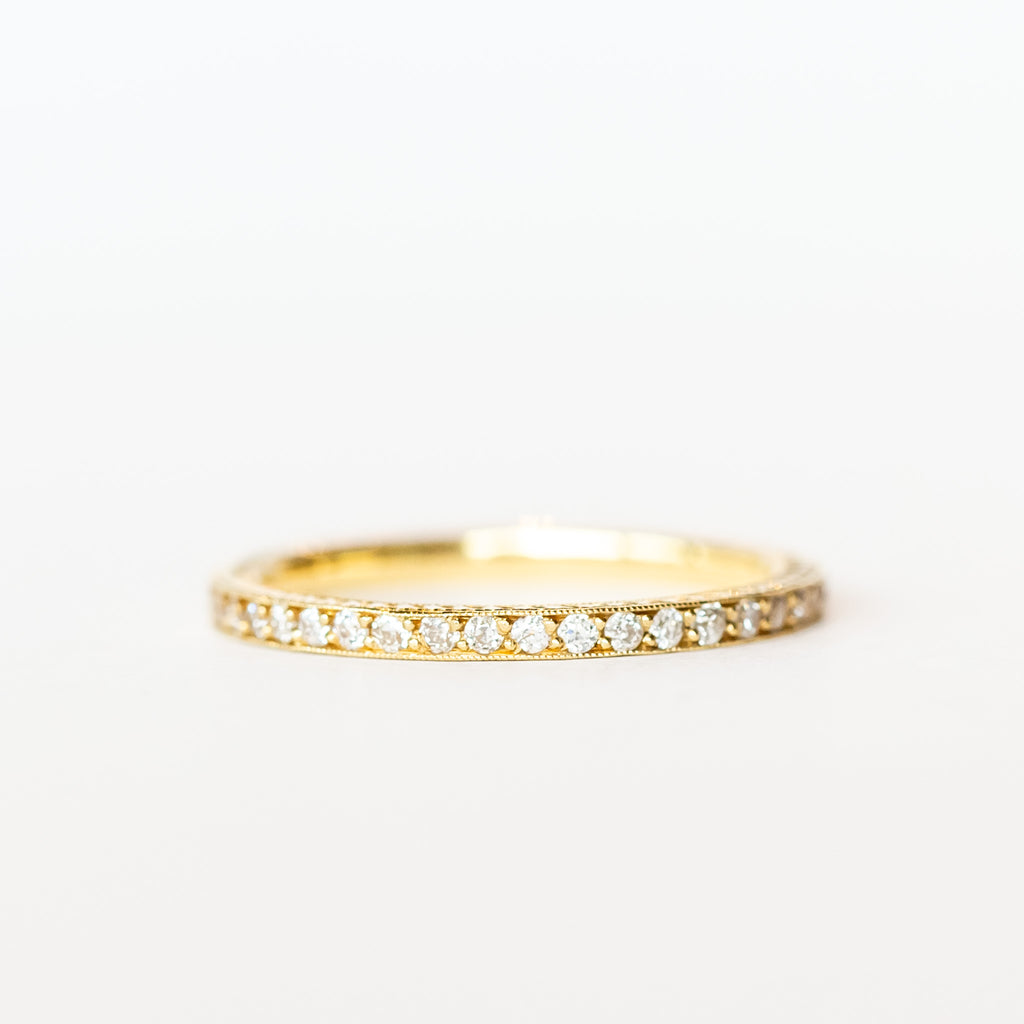 A yellow gold diamond eternity band with a tiny row of diamonds all the way around and engraved sides.
